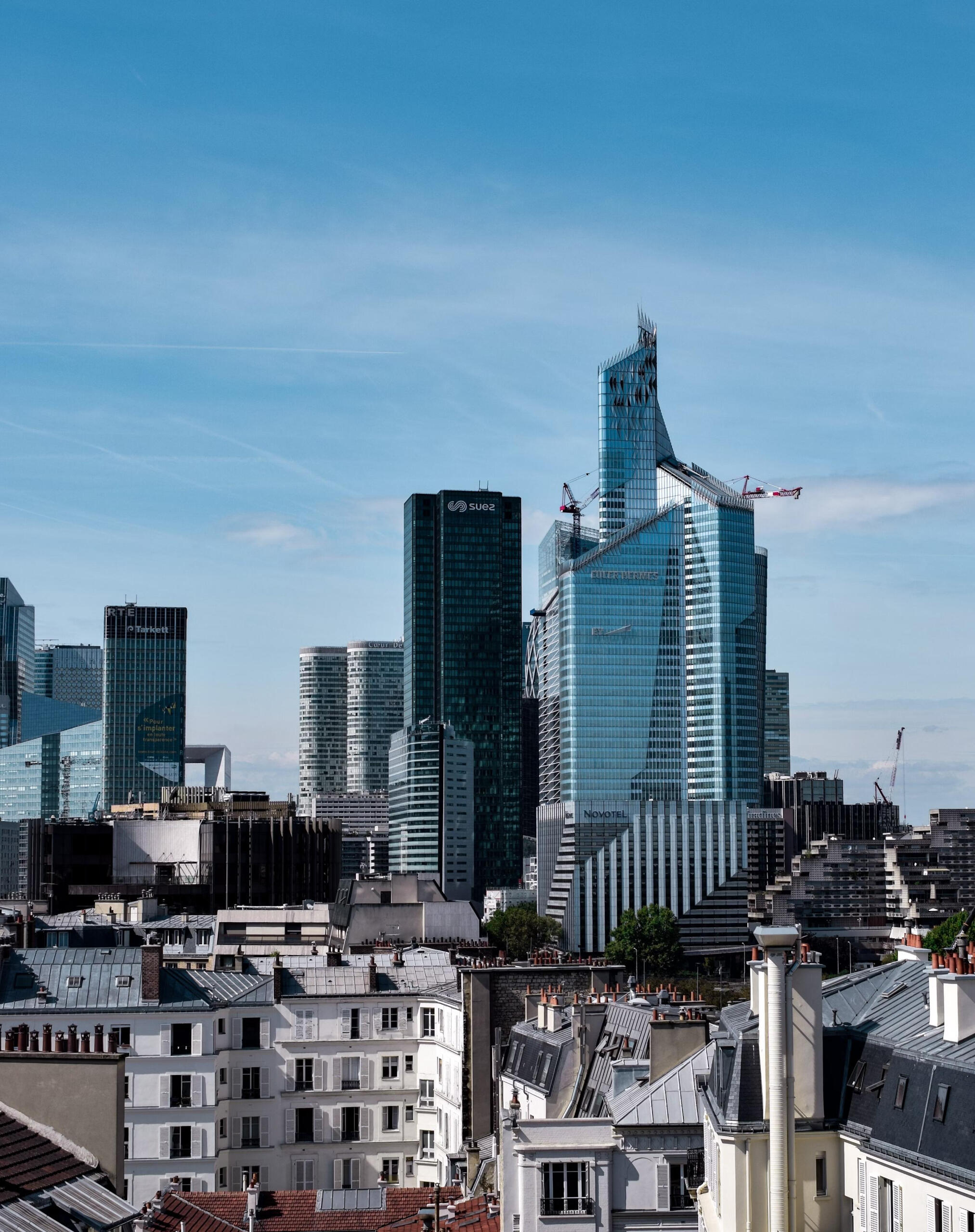 Modern Business Skyline in Paris A panoramic view of Paris blending classic Parisian rooftops in the foreground with the modern glass skyscrapers of La Défense business district in the background under a clear blue sky.